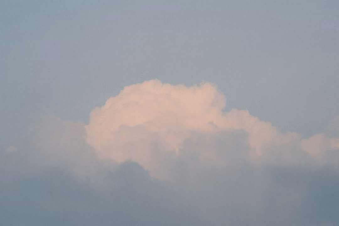 Pale pink cloud drifting low over a grey haze layer in a darkening blue sky