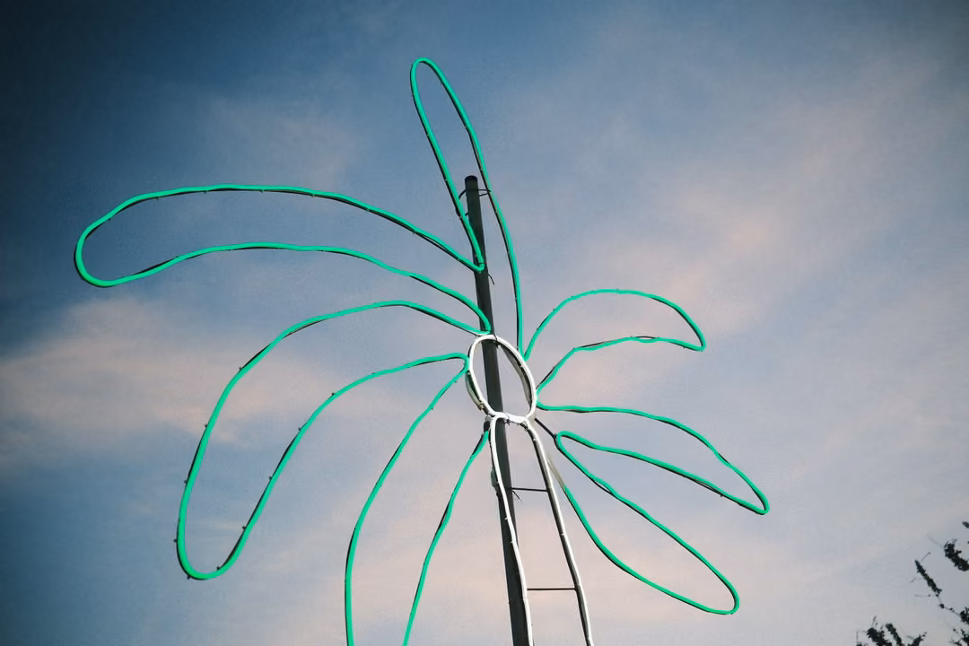 A green neon palm tree outline mounted on a metal pole against a blue evening sky