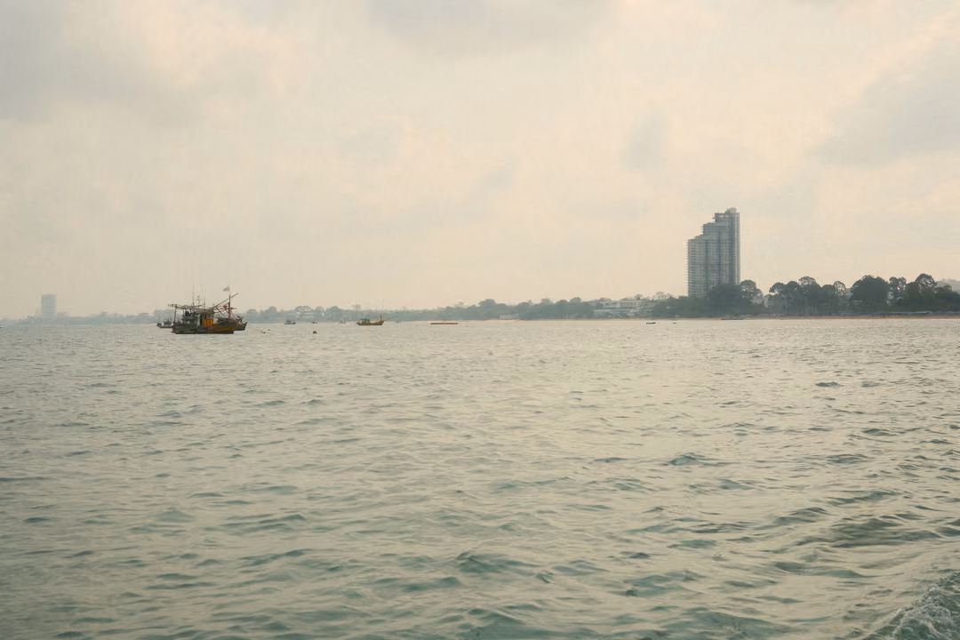 A wide sea with a fishing boat in the middle distance and a tall tower block on the shore to the right.
