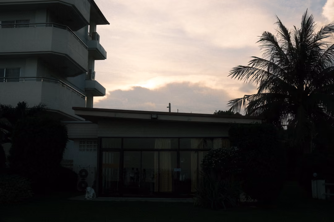 Dark silhouette of a multi-storey hotel building and palm tree against a soft evening sky