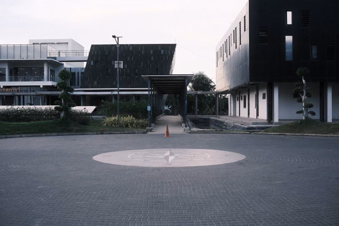 Paved circular forecourt with a compass rose at dusk, modern buildings with dark panels and a covered walkway
