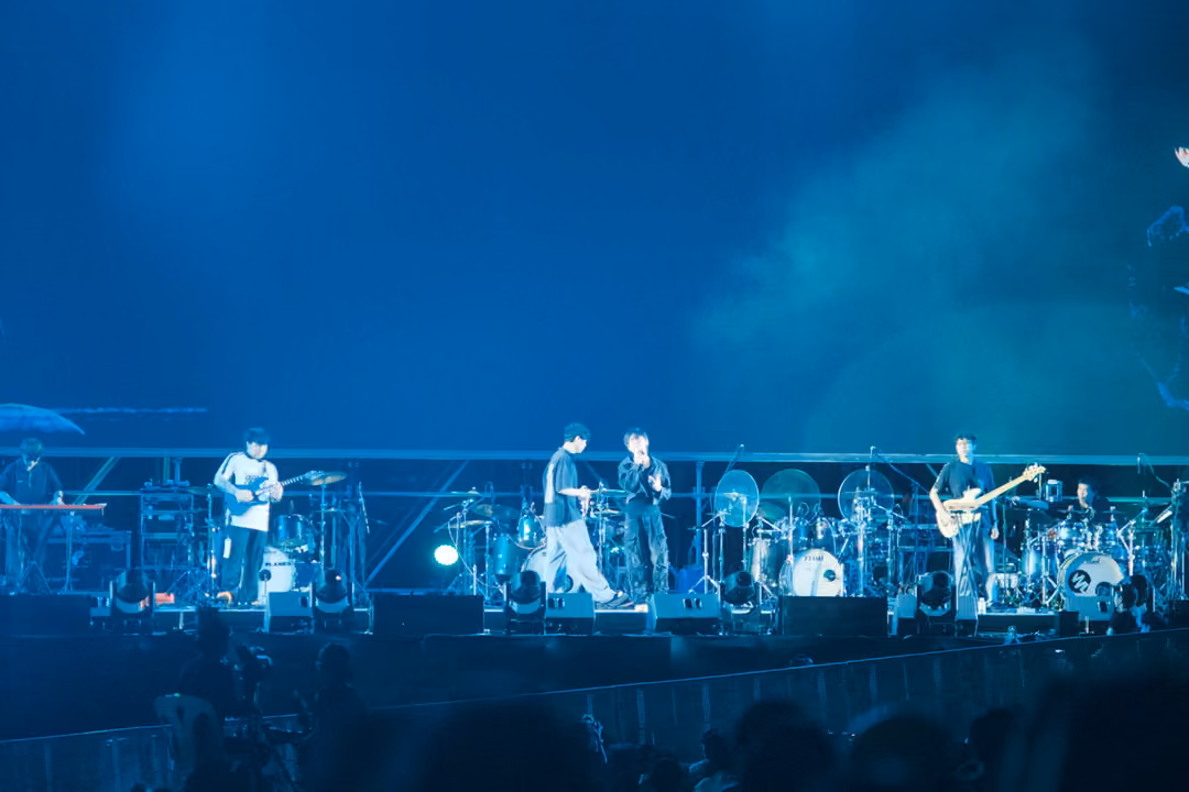 Band performing on a hazy blue stage, white smoke drifting at right, drum kit at centre.
