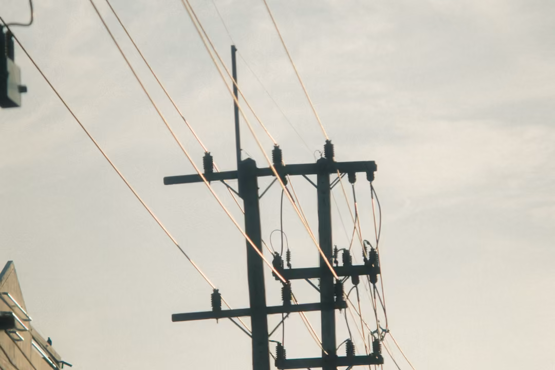 A concrete utility pole with crossbars and diagonal power lines against a pale, hazy sky.