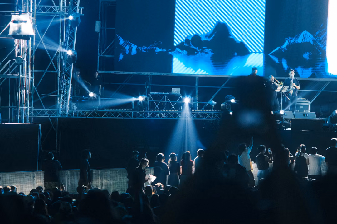 Wide view from the crowd: lighting towers, a blue screen showing a mountain silhouette, people standing in the dark