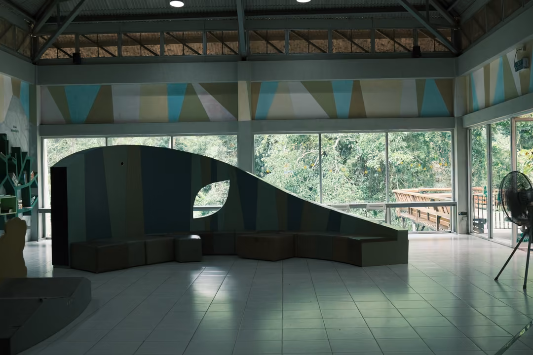 An empty hall with a white tiled floor, a wave-shaped wall with seating and large windows behind
