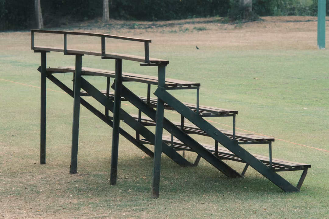 Dark green wooden bleachers with three tiers standing alone on a grassy field