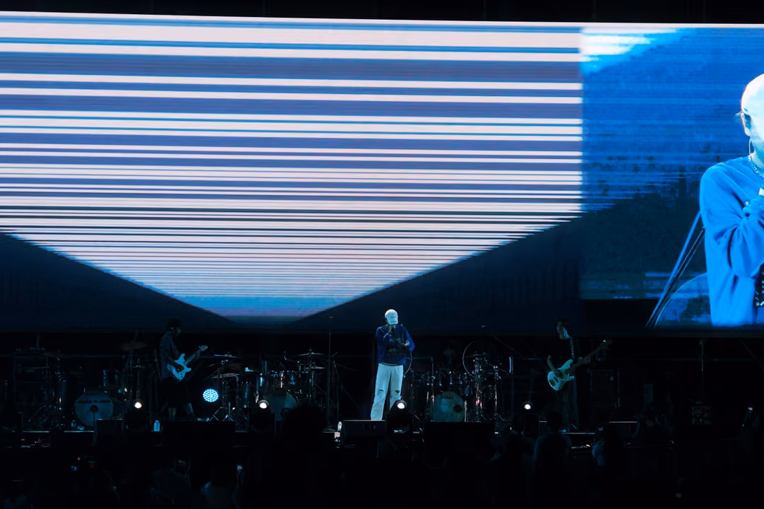 Stage screen showing horizontal white streaks fading into a V shape, the singer in a blue jacket on stage below.