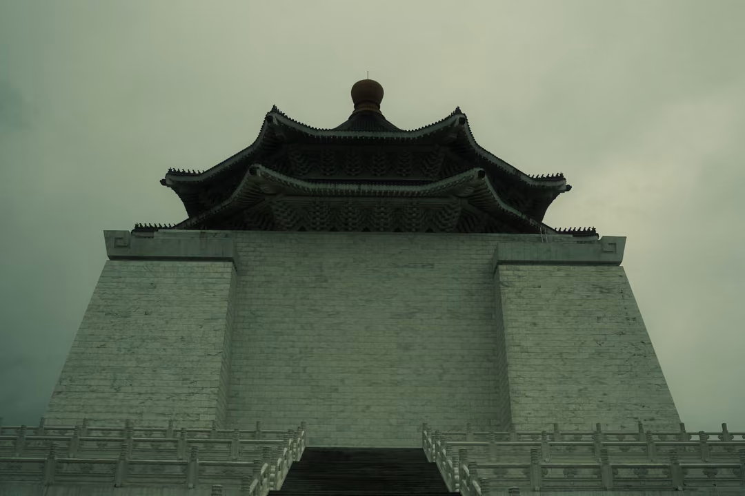 White hall with a dark tiered roof against a greenish stormy sky, viewed from below