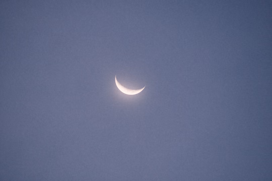 A thin crescent moon low in a dusky blue sky