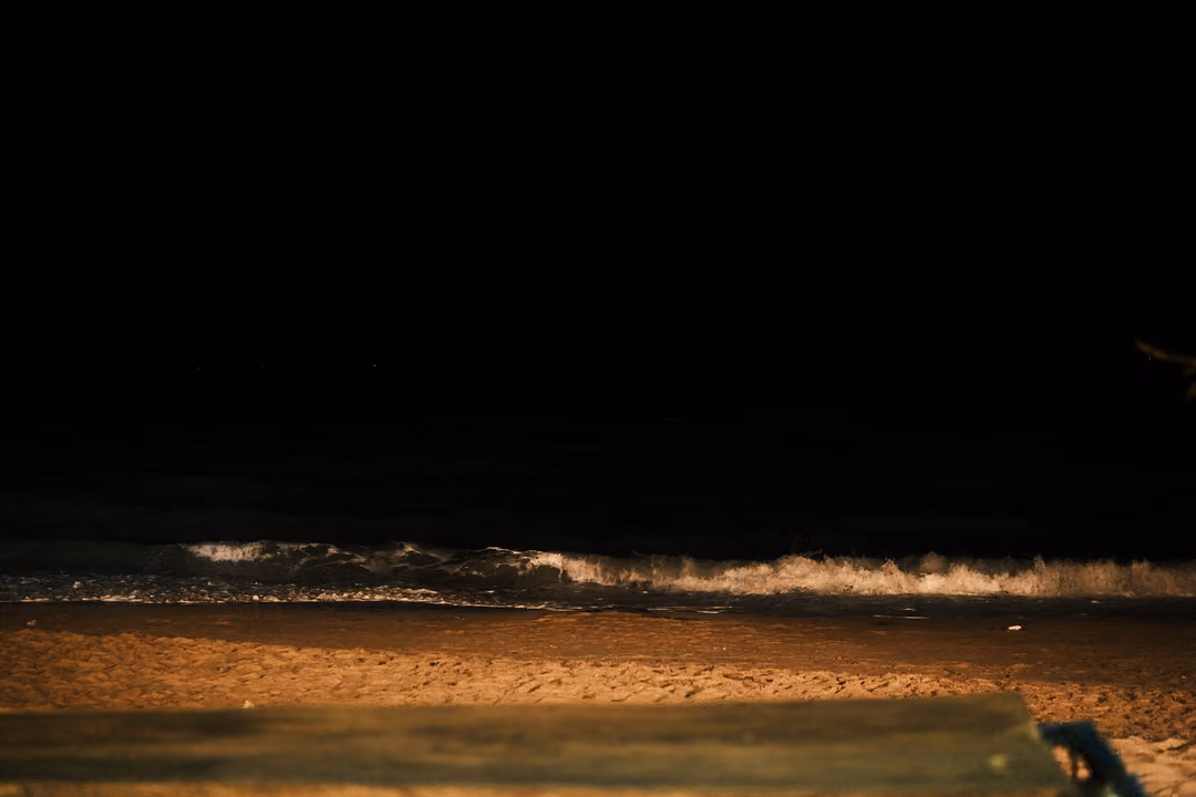 Waves breaking white on a dark beach at night, sand lit warm in the foreground