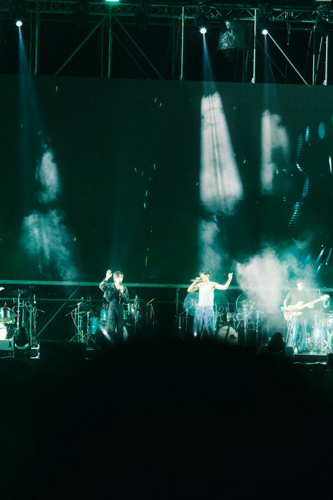 Vertical view of a green stage with white smoke jets bursting upward and the band performing below.