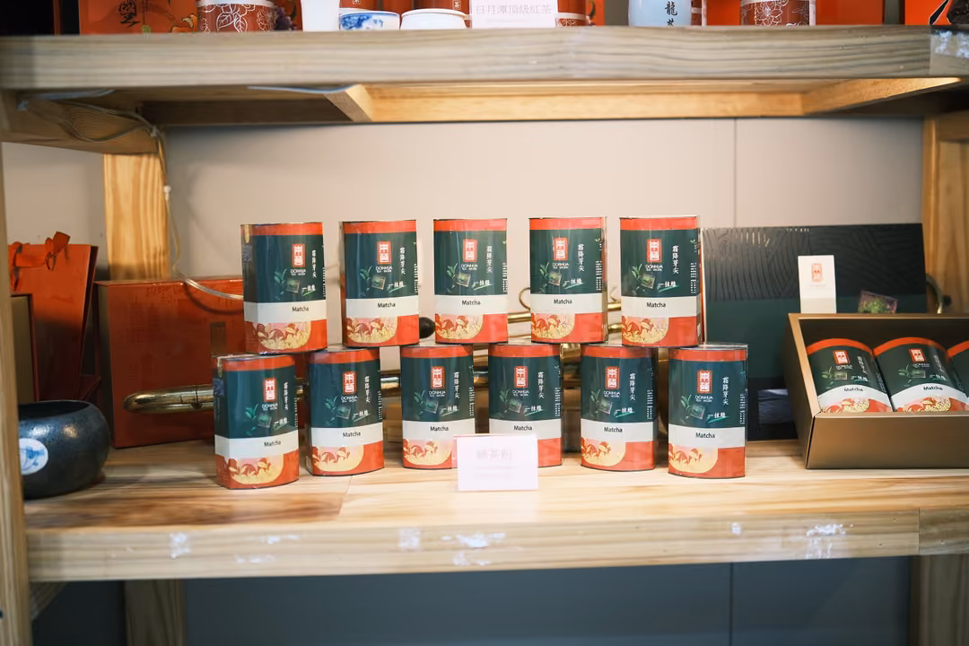 Shop shelf stacked with green and red tea tins in two rows, gift boxes and bags on either side