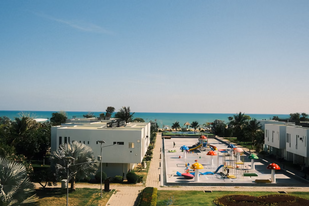 Elevated view of white villas around a colourful splash park, palm trees and a turquoise sea behind