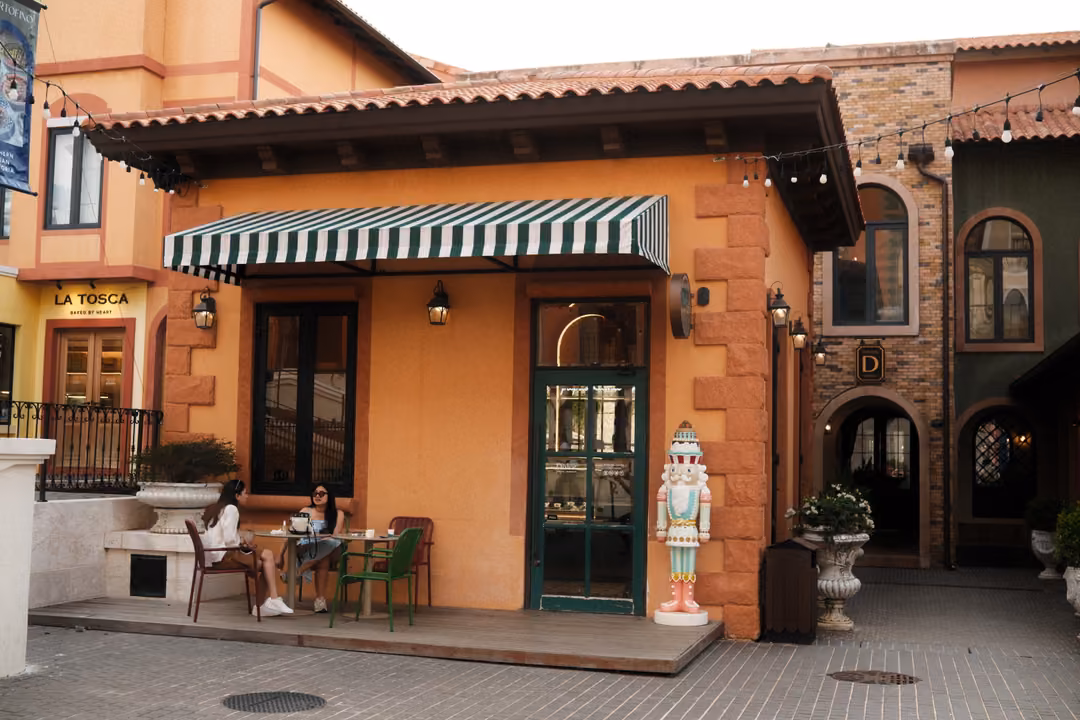 Small café with a green striped awning and La Tosca sign, a nutcracker figure by the door and two people at a table