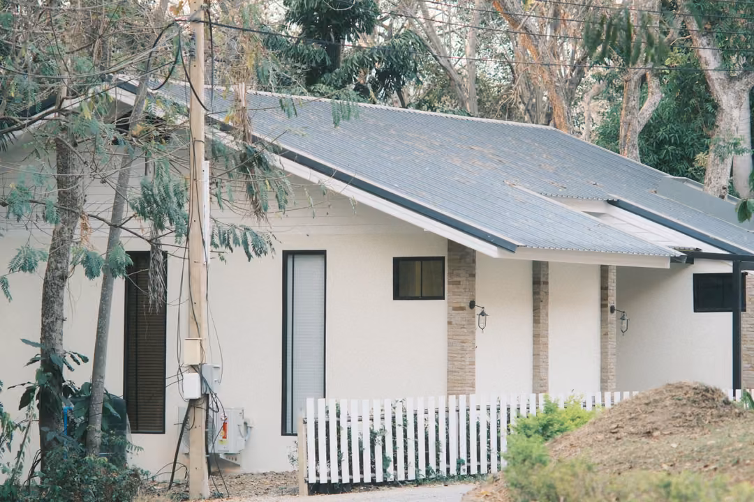 White house with a grey metal roof and a white picket fence, a mound of earth and bare trees around it