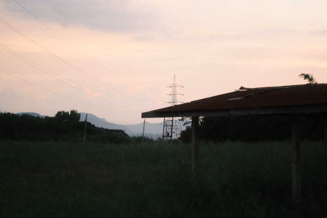 Silhouette of a shelter roof and a distant pylon against a pink sky, dark grassy field below
