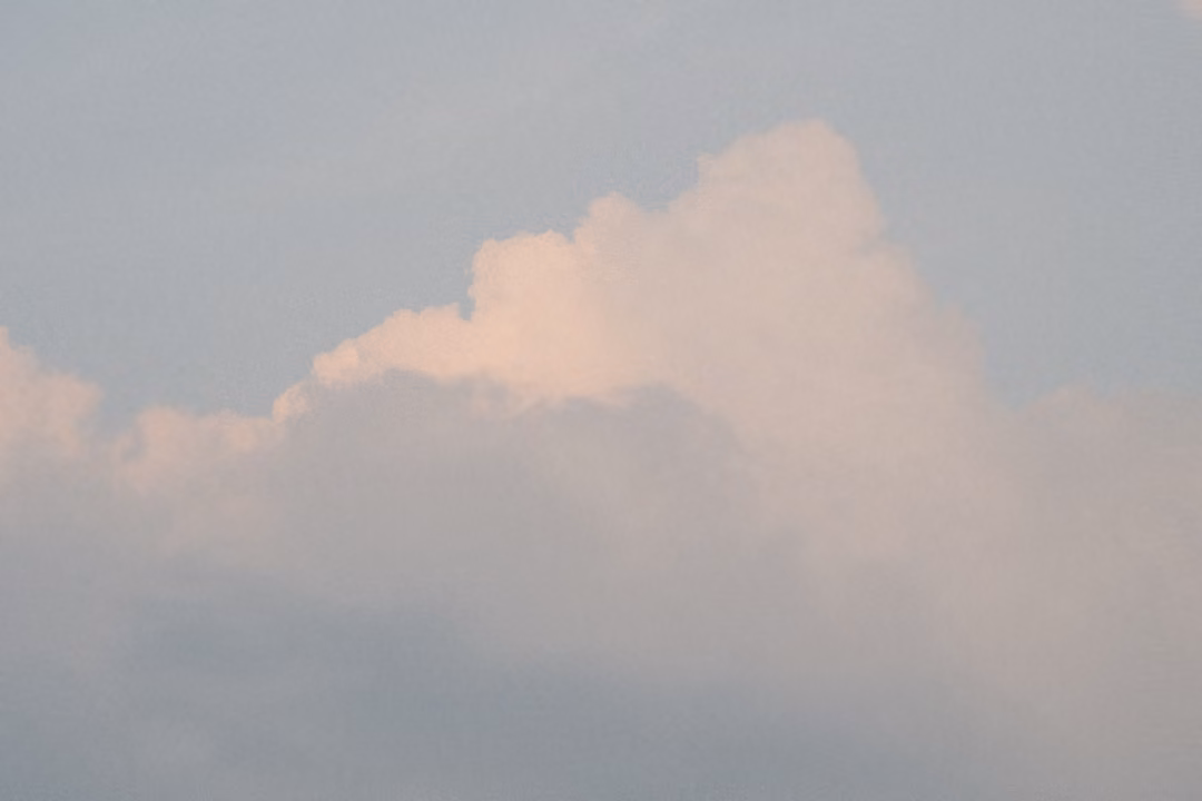 Pink-lit cloud tops rising above a grey band of haze in a blue-grey evening sky