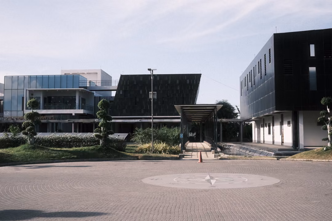 Circular paved forecourt with a compass rose inlay, modern buildings with dark angled roofs and a covered walkway