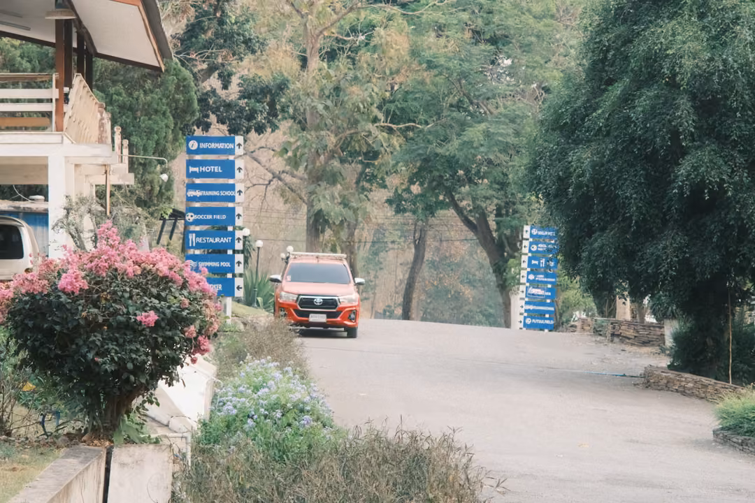 Orange pickup parked on a driveway beside blue direction signs and a pink bougainvillea bush