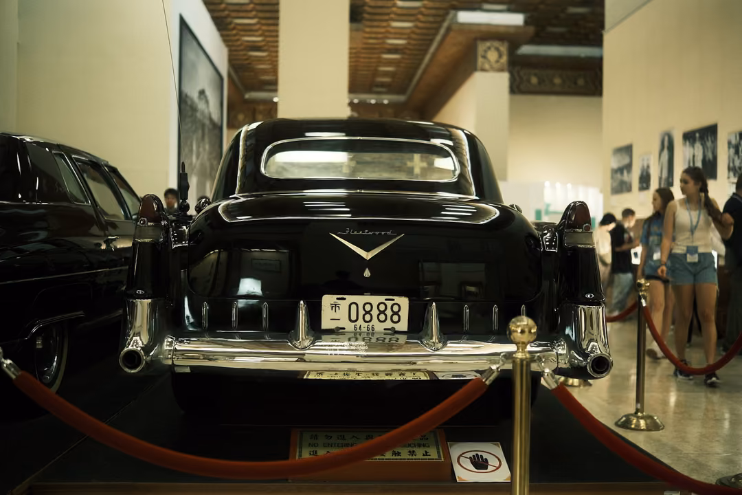 Rear of a black vintage car with chrome fins and plate 0888, visitors walking past along a roped path