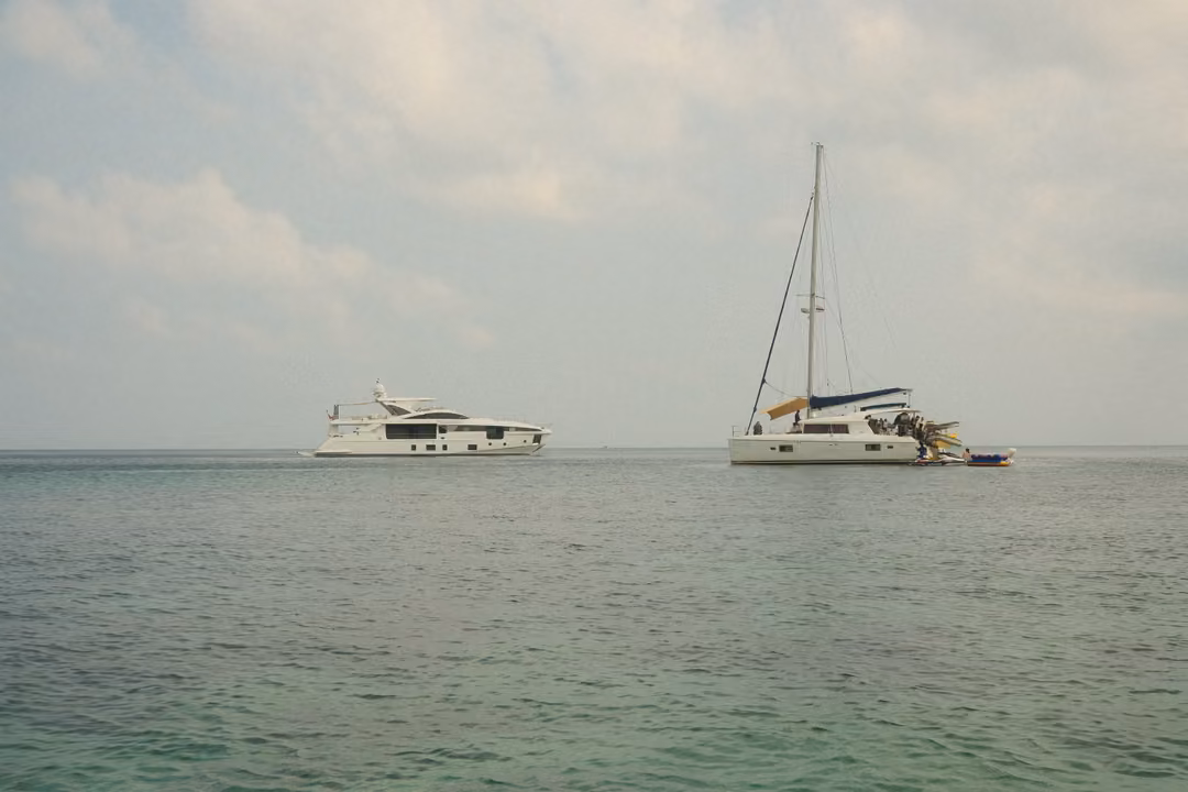 A white motor yacht and a catamaran sailboat anchored side by side on calm sea.