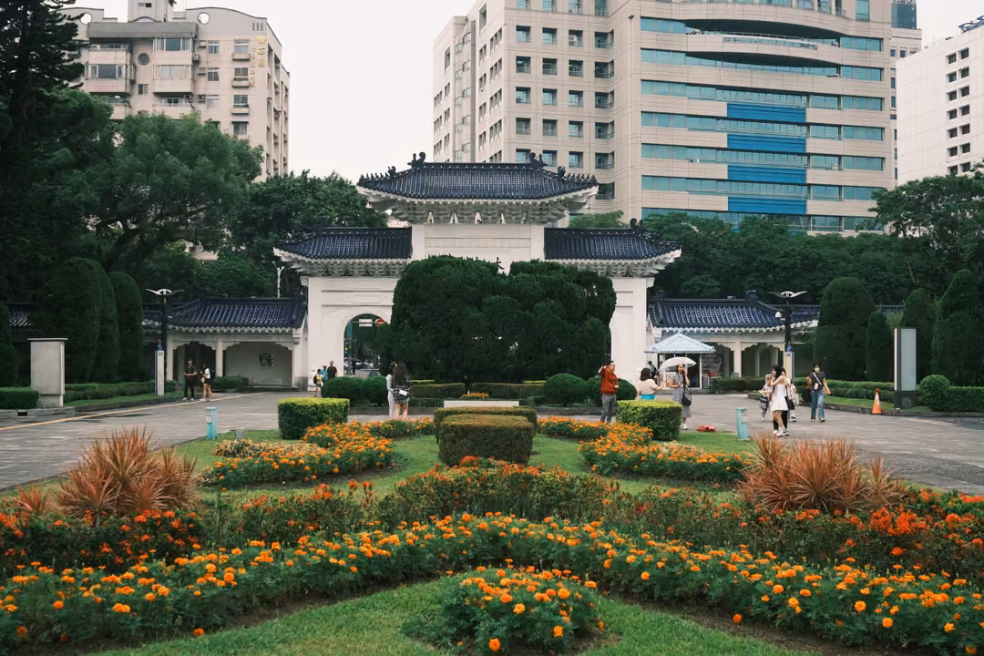 Formal garden with orange and yellow marigolds and clipped hedges, a white gate with blue roofs and towers behind