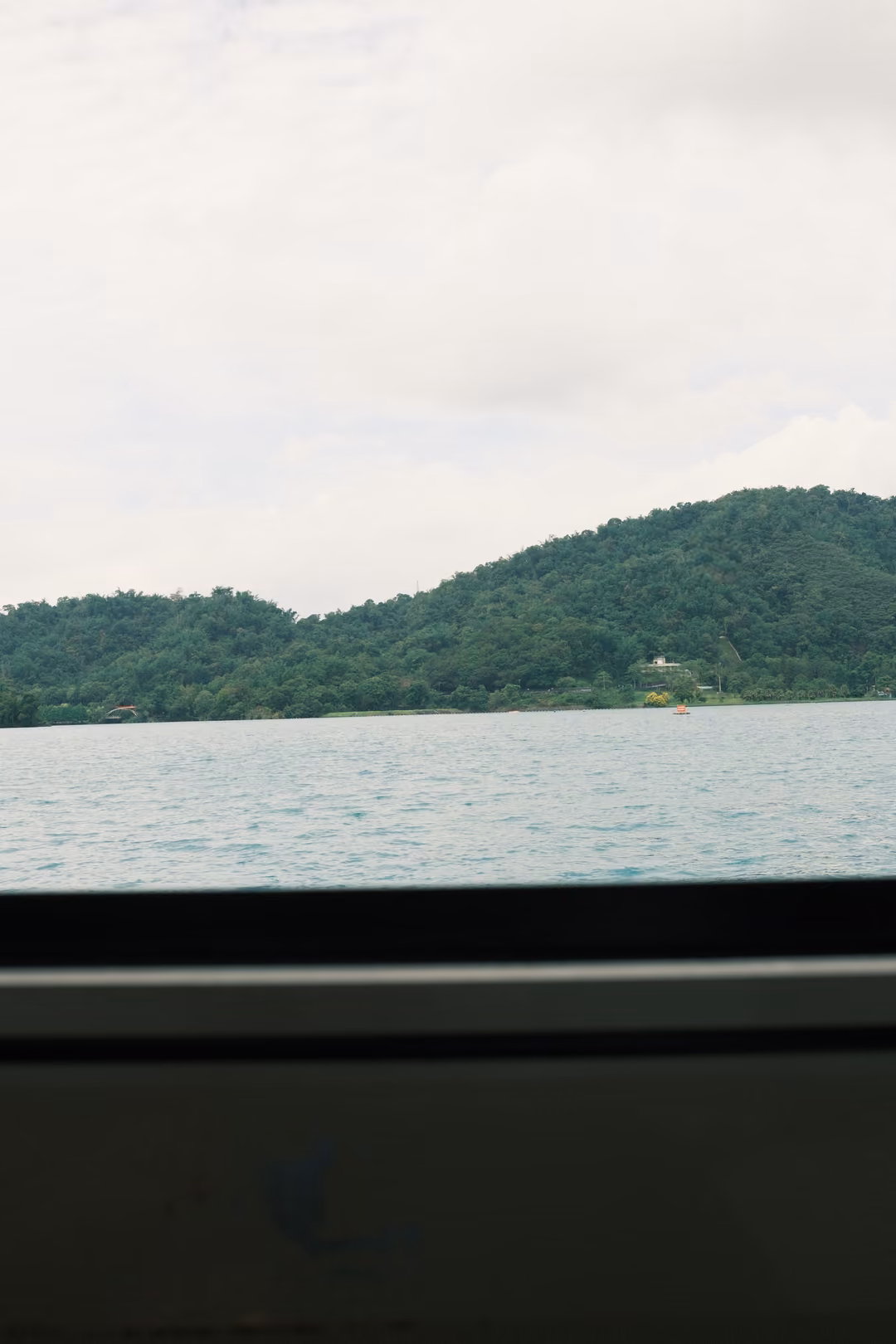 Green hills and lake seen through a boat window, the dark window frame filling the lower half
