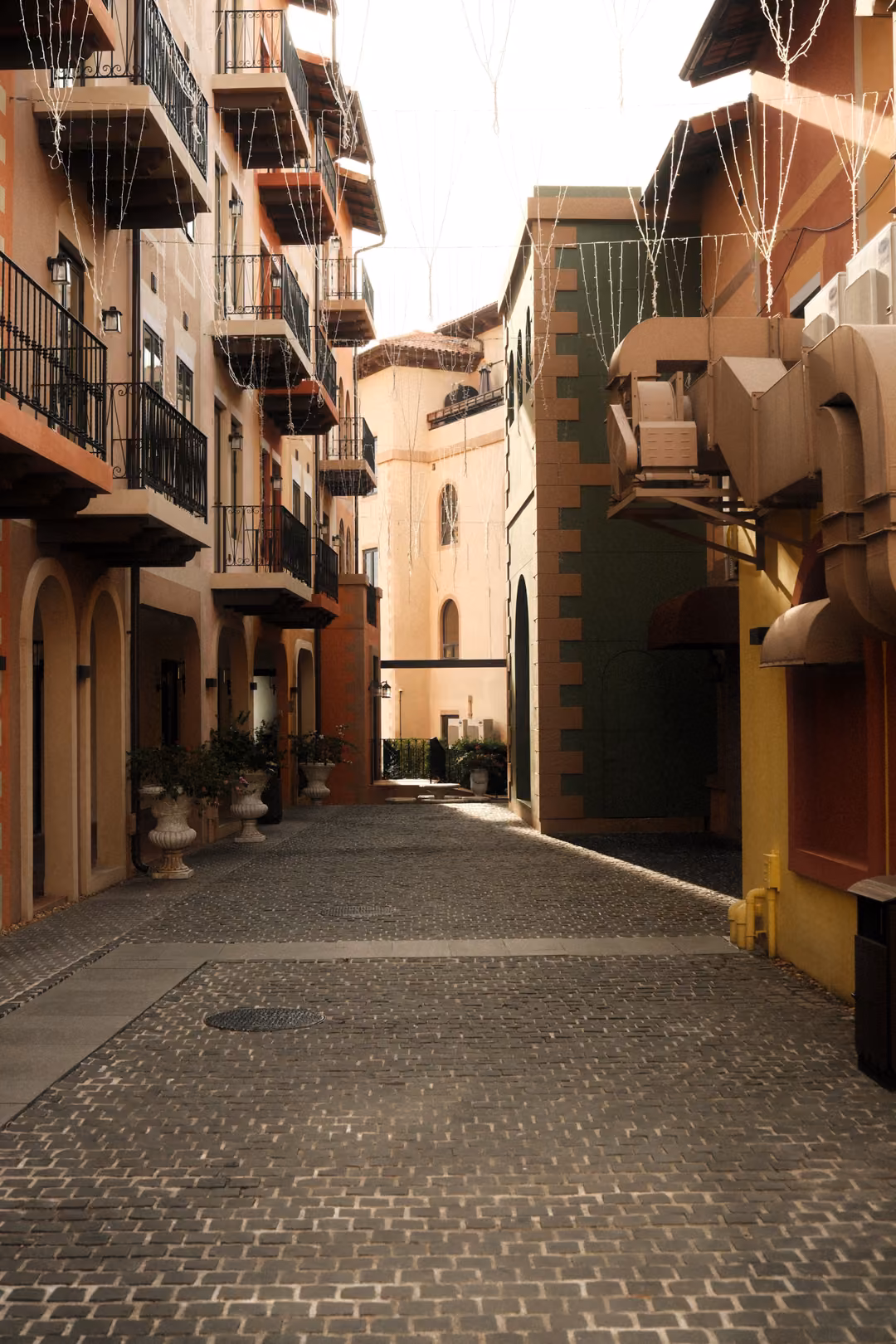 Narrow cobbled lane between pastel buildings with iron balconies under a bright, overcast sky