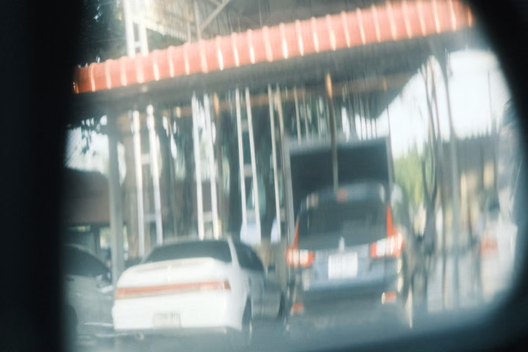 A round convex mirror reflecting white sedans and a dark van parked under a canopy with a red edge.
