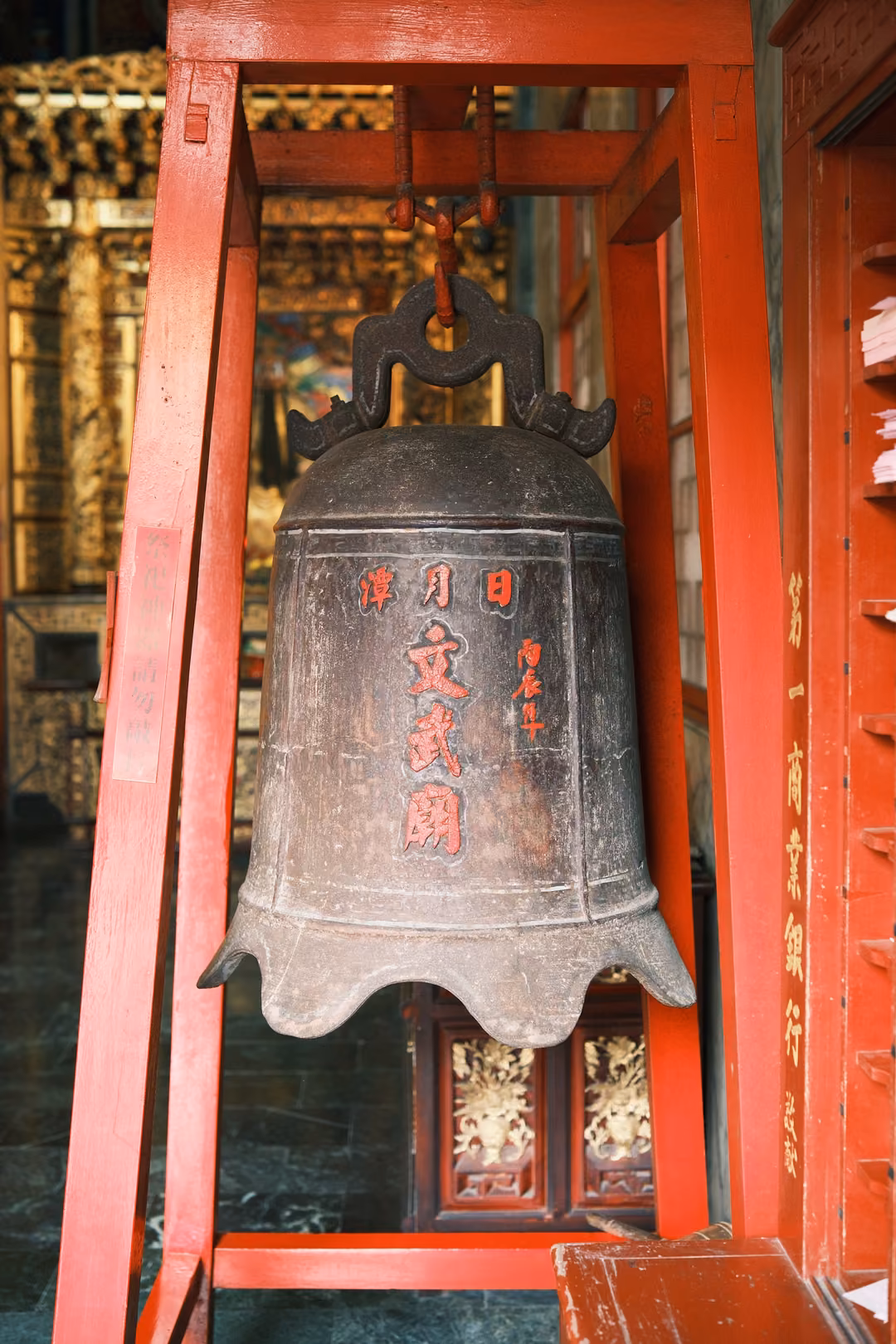 Old bronze bell with red characters hanging in a red wooden frame inside a temple hall