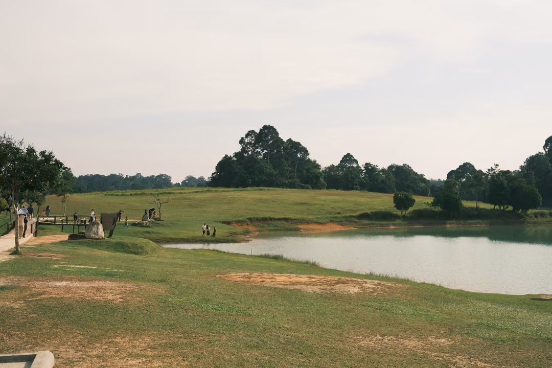 A green lakeside lawn with a wooden viewing deck, a few visitors and trees along the water.
