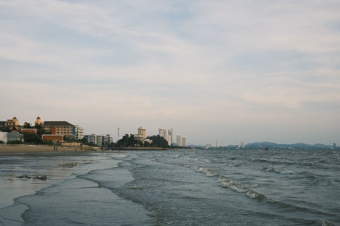 Low waves rolling onto a long beach lined with hotels and towers under a pale blue sky
