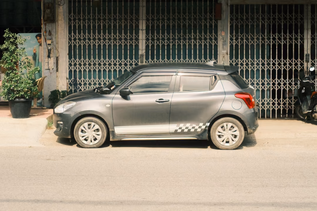 A grey hatchback with a checkered stripe parked in front of closed metal shutter doors on a quiet street