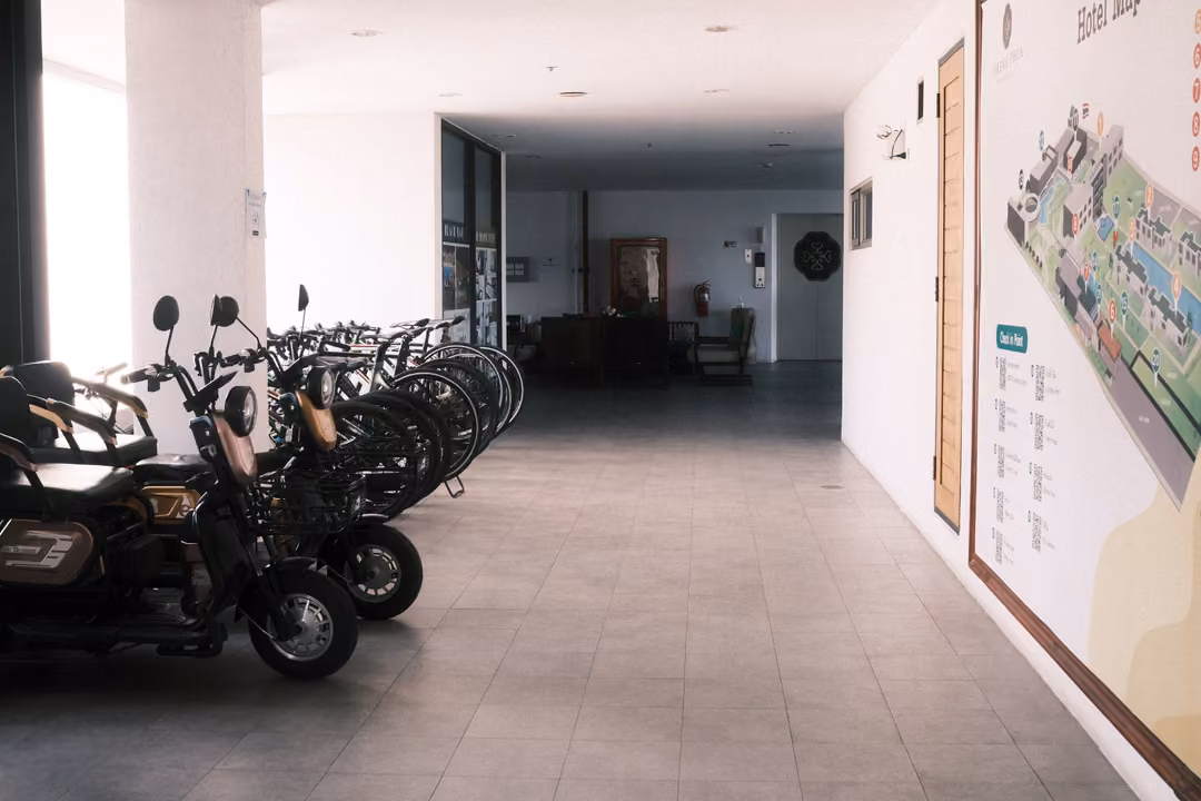 Indoor corridor with electric scooters and bicycles parked against a wall, a large resort map on the right