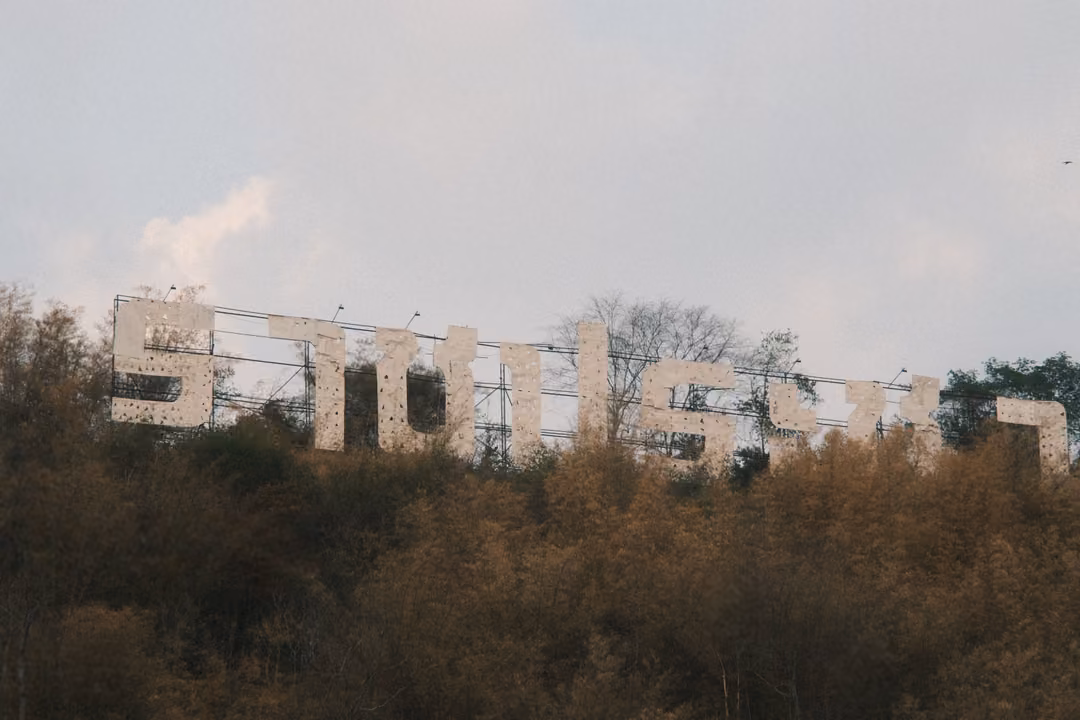 Large white Thai letters standing on a hillside above dry brown trees, under a pale sky