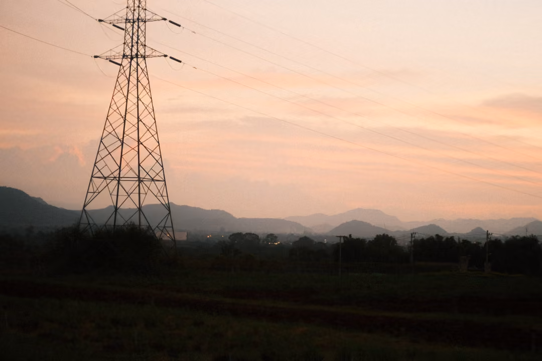 Tall electricity pylon at the left against a pink sky with distant mountain range, dark fields below