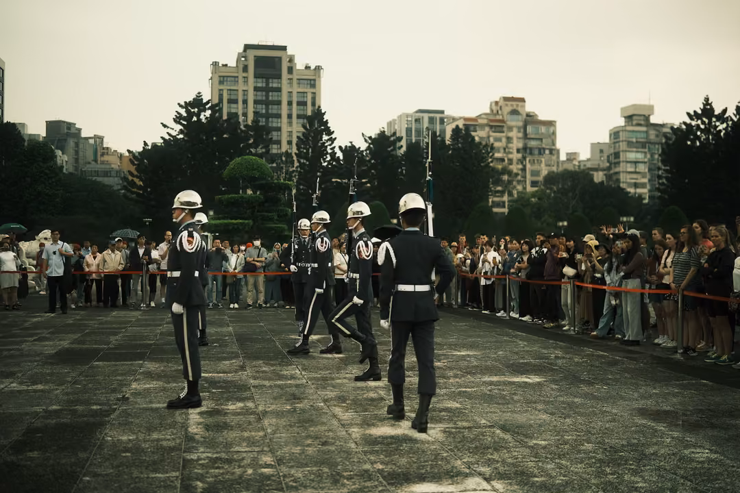 Honour guards in white helmets marching in formation across a plaza, spectators watching behind a rope