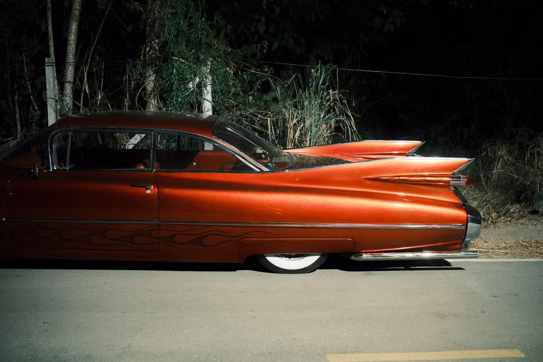 Glossy red vintage car with tall chrome-trimmed tail fins parked on a dark roadside at night