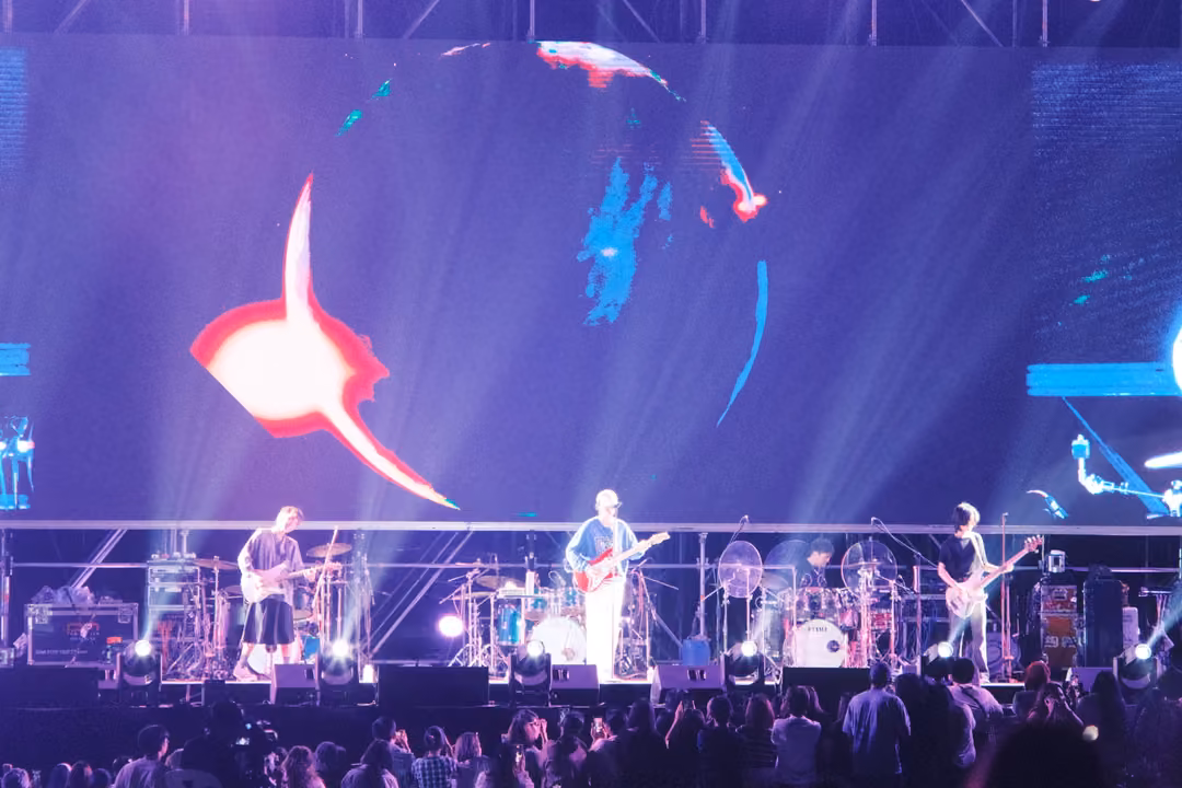 Band on a purple stage under a screen showing the outline of a sphere and a bright red flare at left.