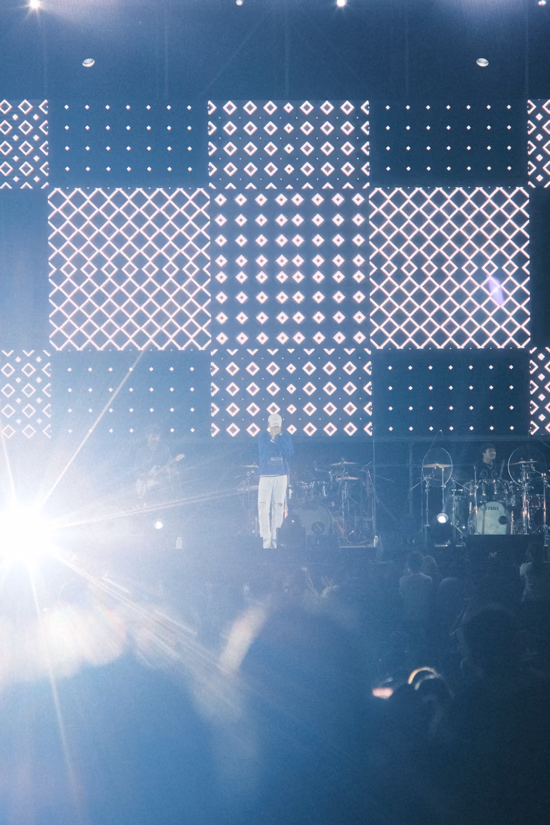 Vertical view of a stage with a huge starburst lens flare at lower left, the singer small under a screen of diamonds.