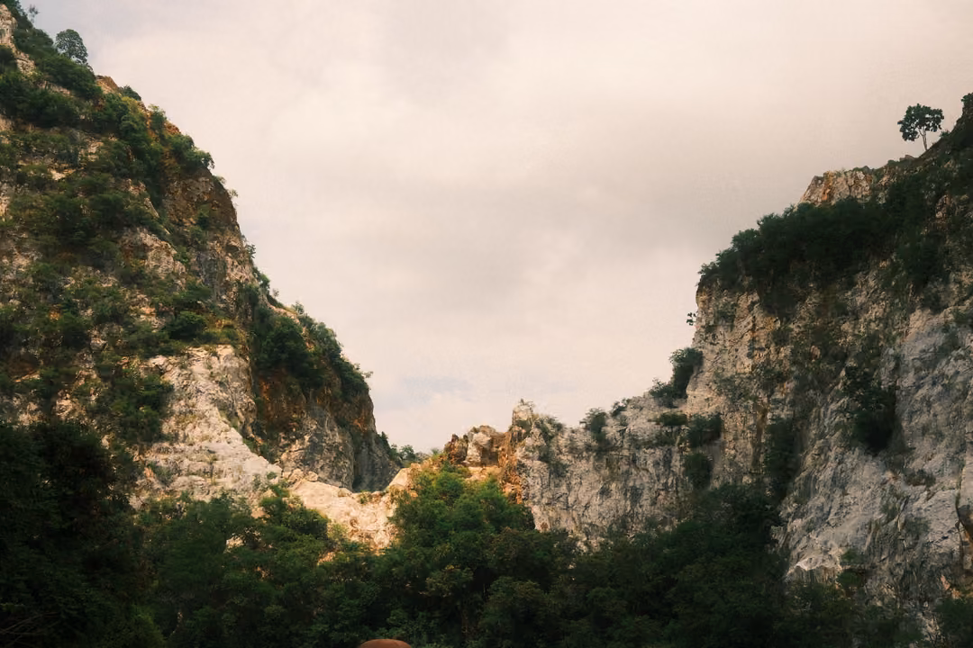 Two dark, tree-covered cliff faces forming a V-shaped gap against an overcast sky
