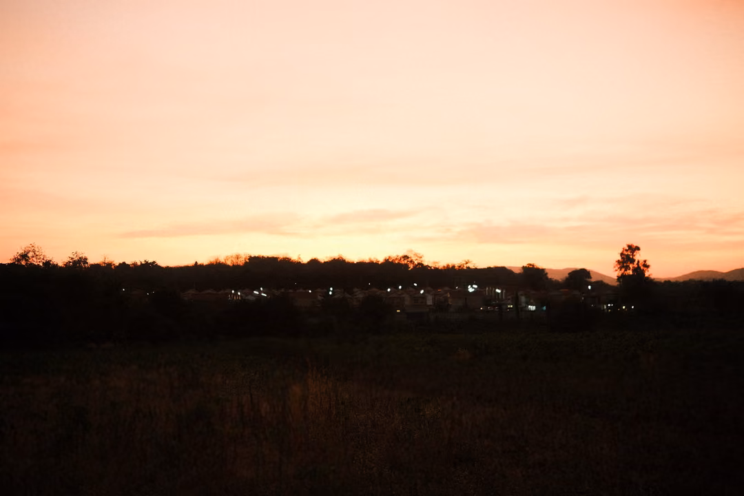 Orange and pink sunset sky over a dark horizon, lights scattered along a distant line of houses