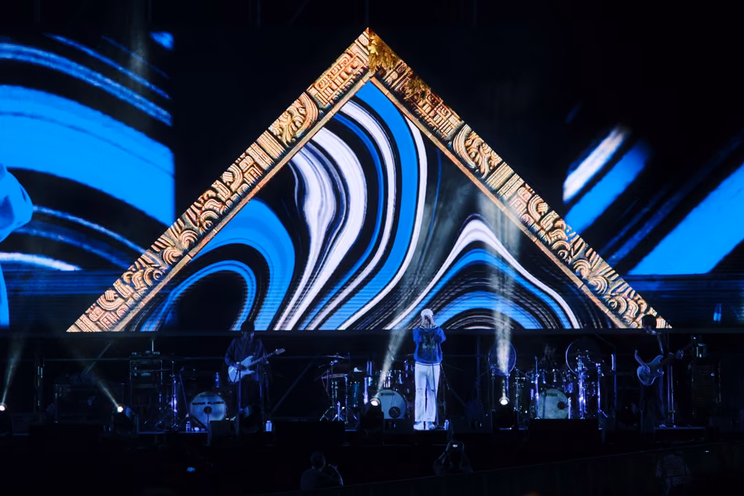 Band beneath a gold-framed triangle of blue and white swirling bands, white smoke rising beside the singer.