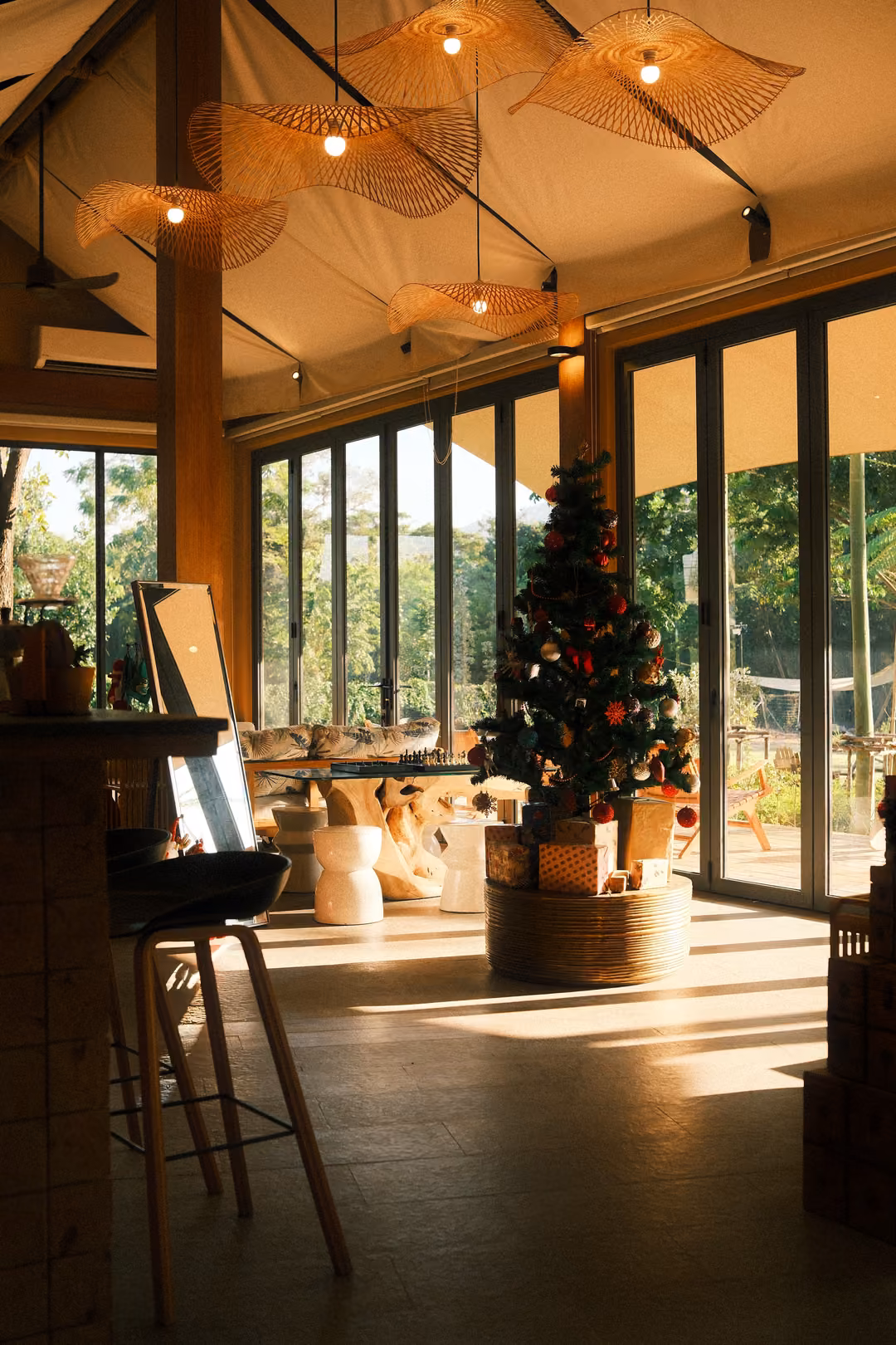 High-ceilinged café with woven pendant lamps, a Christmas tree by the windows, bar stools and sunlit floor