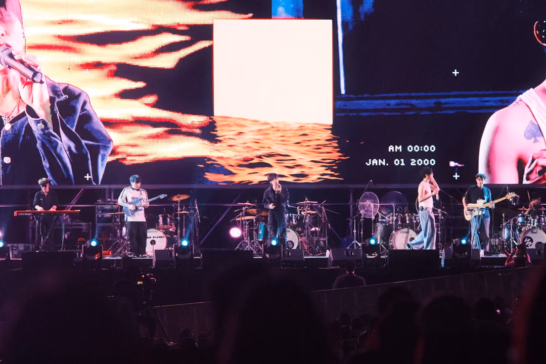 Band performing under a screen showing orange waves, a white square and a date stamp reading JAN. 01 2000.