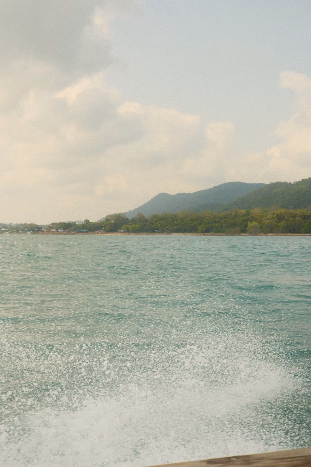 Spray and foam from the boat's wake, with green hills along a distant shoreline under blue sky.
