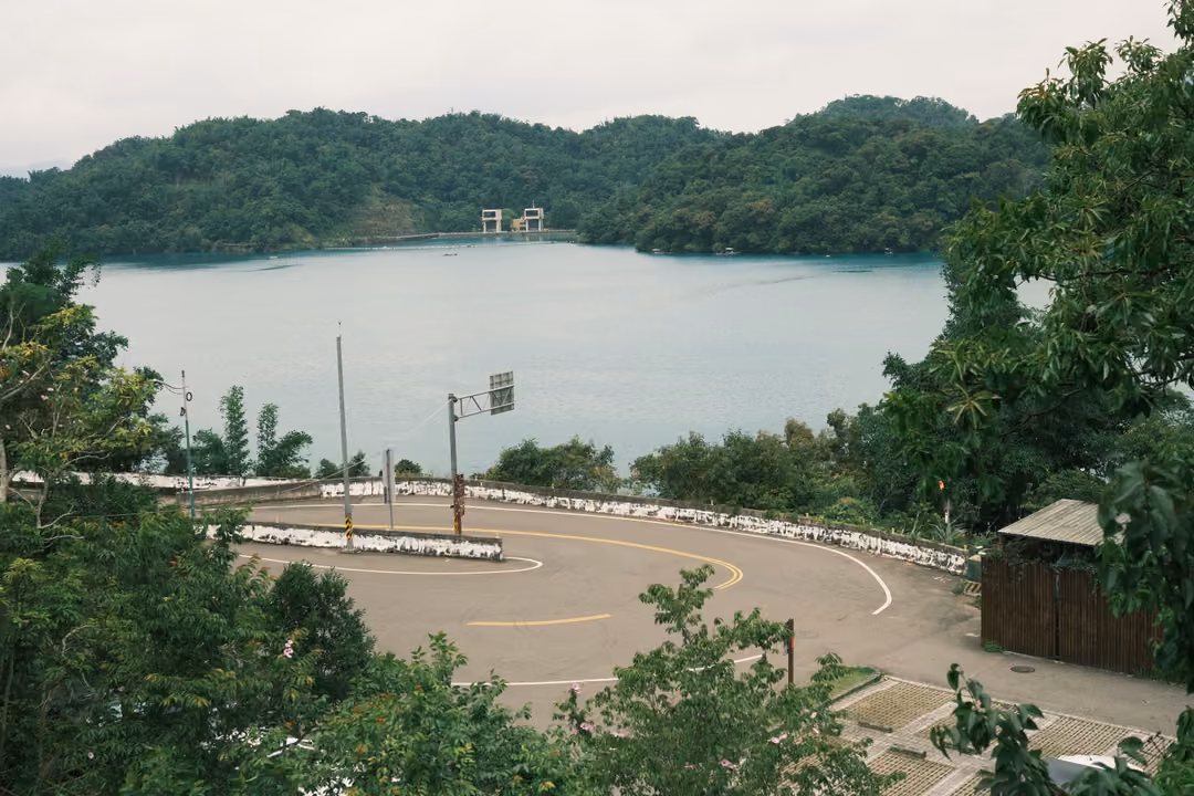 Curving road with a turnaround and roadside signs above a lake, forested hills on the far shore