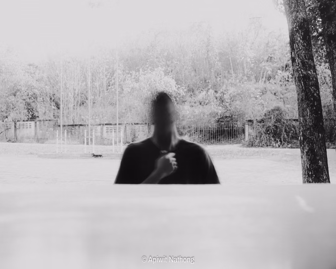 Black and white image of a figure in a dark shirt with a blurred face standing on a bare open ground