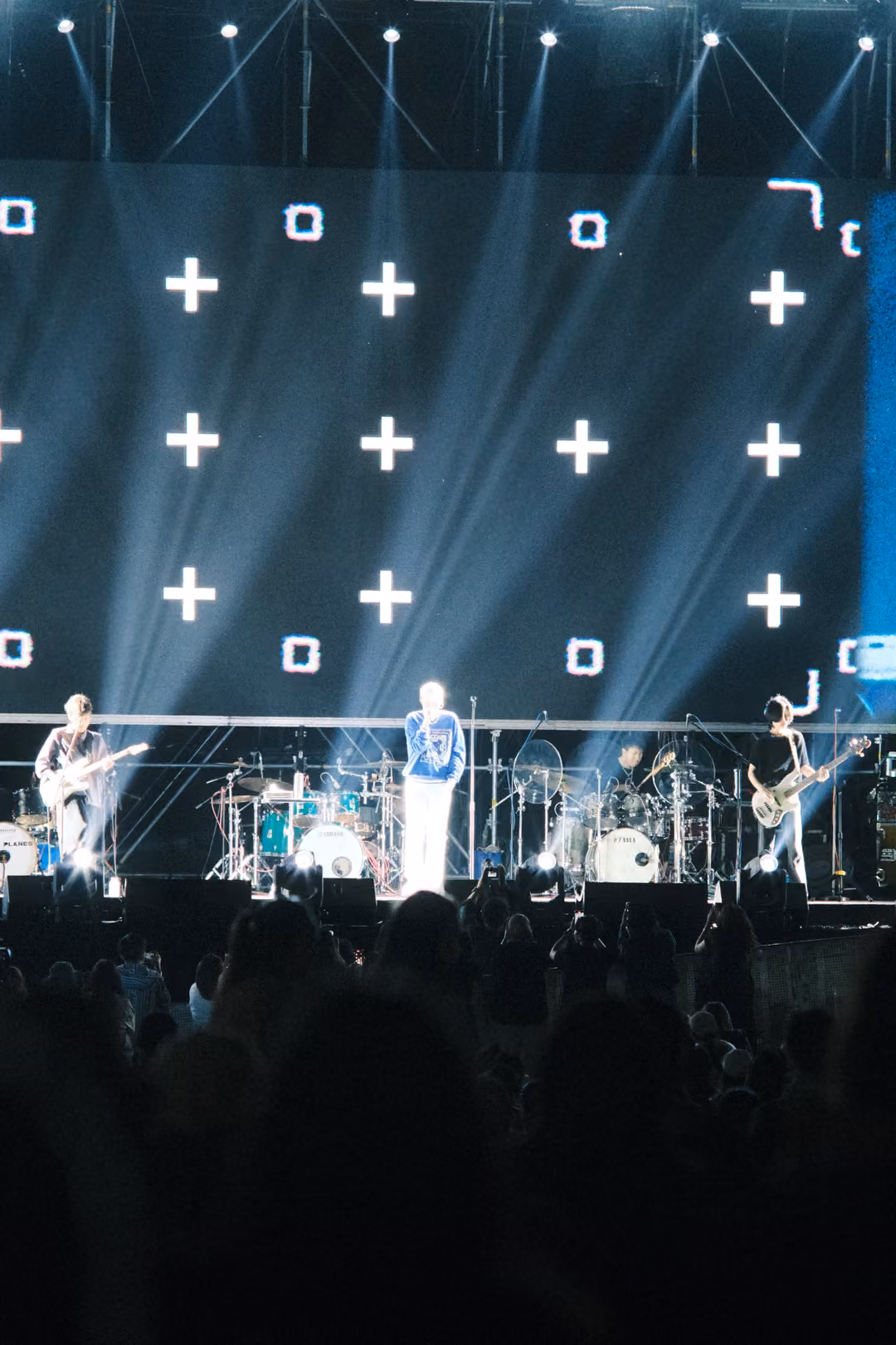 Vertical view of a screen of white plus signs and small squares, beams of light, the singer in a blue jacket on stage.
