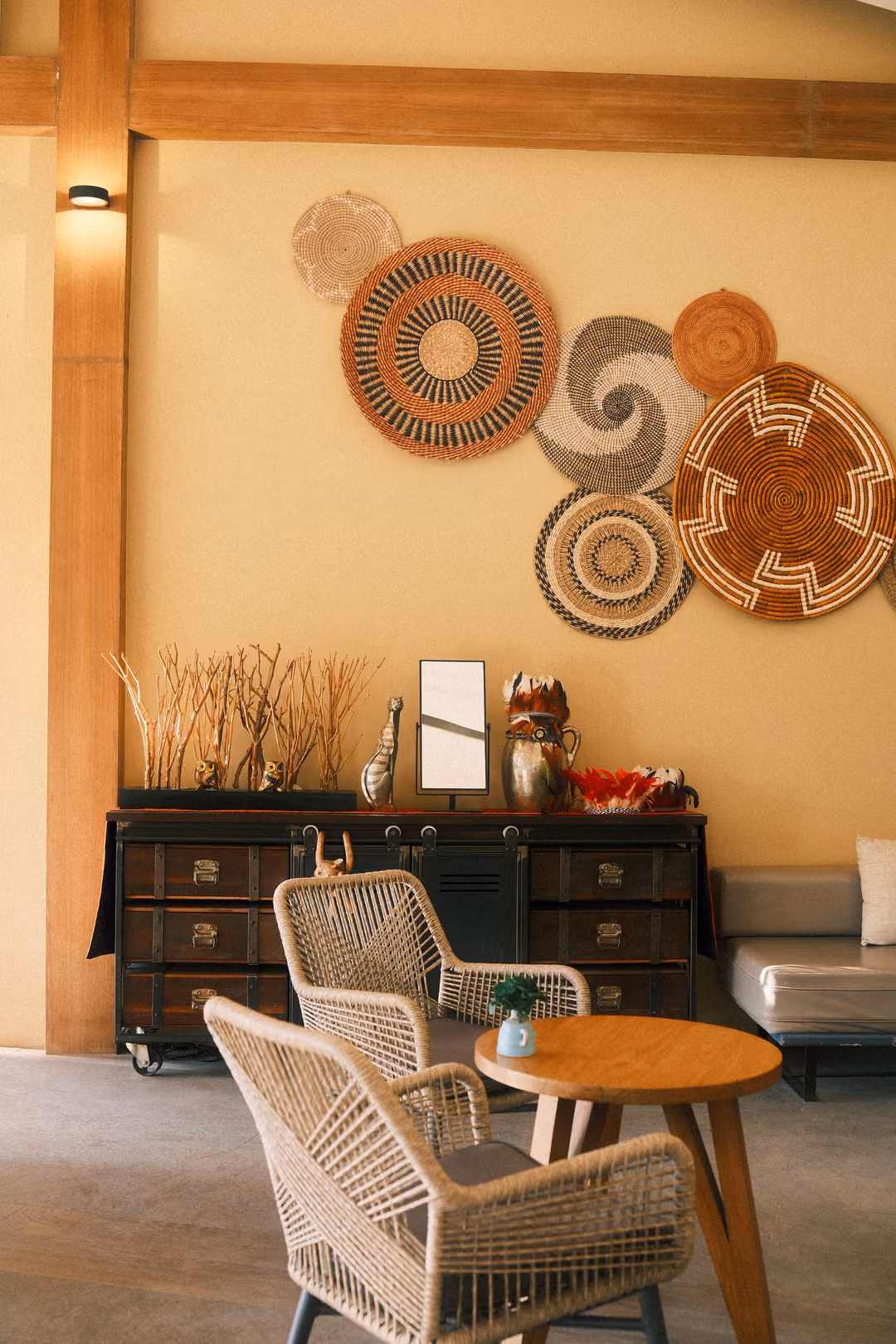 Café corner with woven baskets on a yellow wall, a dark cabinet, wicker chairs and a small round table